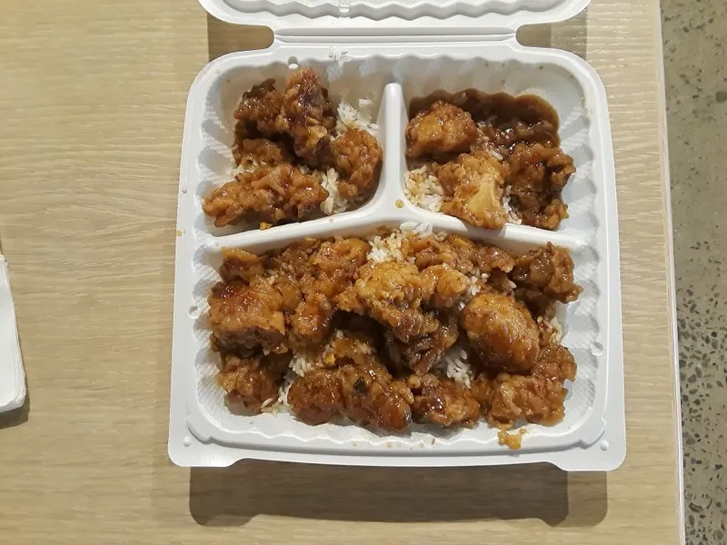 Orange chicken over rice in a white foam clamshell.