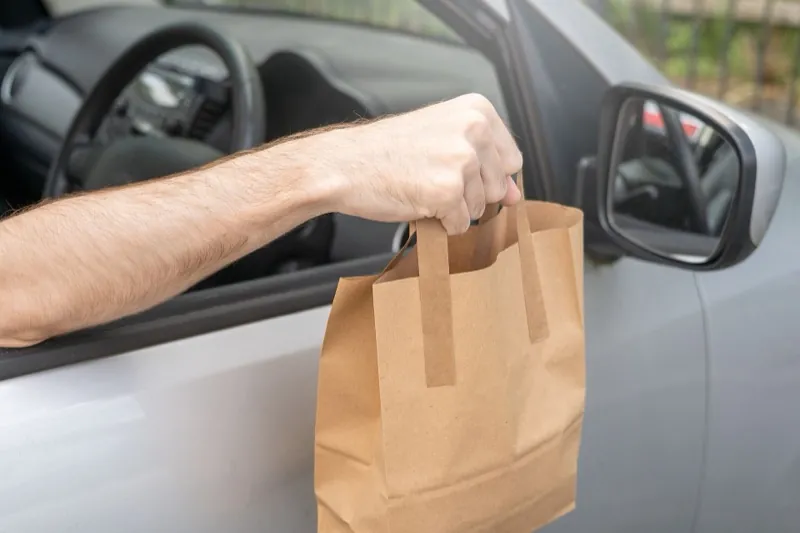 A paper takeout bag handed through a car window.