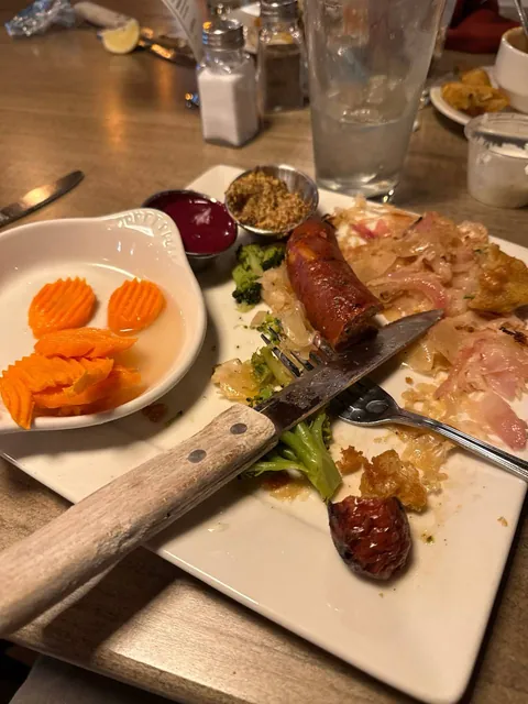 The same plate after eating: one sausage end, some kraut and broccoli, and a few carrot chips left.